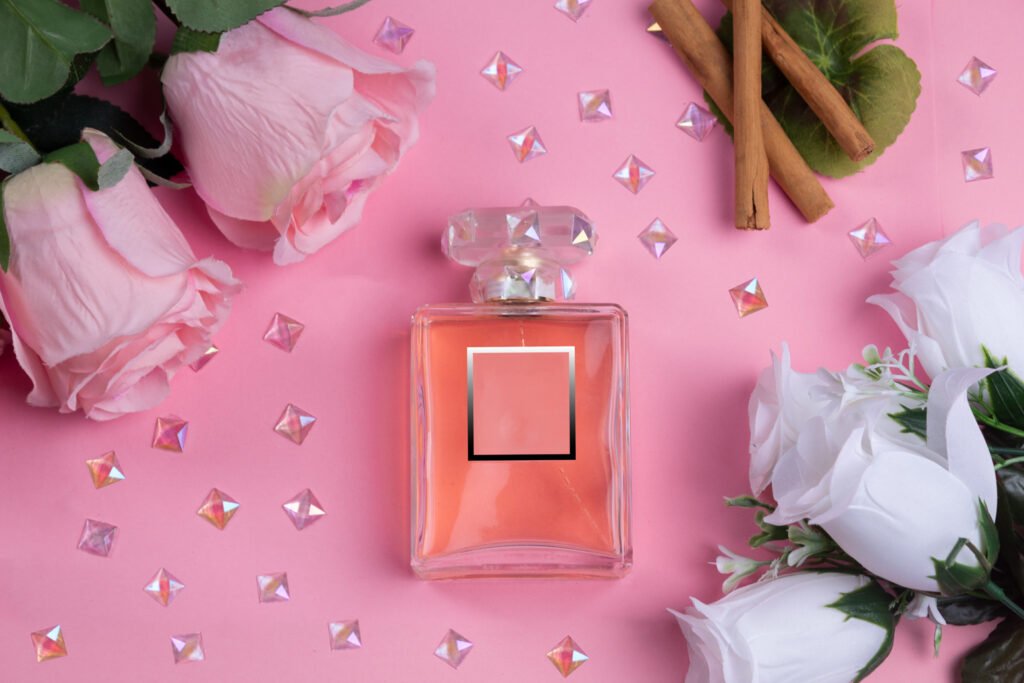 Perfume y brilli brilli, una foto compuesta del mismo bote de la foto perfume, pero tumbado sobre una cartulina rosa y rodeado de diamantes y flores rosas y blancas